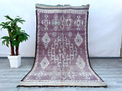 Elevate your home with this rare vintage Beni M’Guild Moroccan rug, showcasing intricate geometric designs in muted purple and neutral tones. Handwoven by Berber tribes using centuries-old techniques, this 6x11 ft wool rug boasts a durable, shaggy pile and organic imperfections that reflect its artisanal origins. The tribal motifs and faded hues create a timeless boho aesthetic, blending seamlessly with mid-century, Scandinavian, or eclectic styles. Perfect as a living room centerpiece or bedroom accent, th