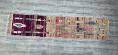 Bring rustic charm into your home with this antique Moroccan Azilal runner rug, a hand-knotted wool masterpiece (approx. 2.3 x 10.9 ft). Featuring a vibrant, faded palette of purples, reds, and neutrals, this vintage Berber rug showcases geometric motifs and organic imperfections that tell a story of nomadic craftsmanship. The plush, high-pile weave offers luxurious comfort, while the durable construction ensures longevity. Perfect for bohemian, farmhouse, or global-inspired décor, this handmade runner adds