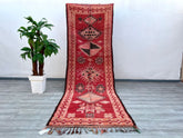 Discover the allure of this antique Moroccan runner rug, a stunning handwoven Berber carpet that exudes vintage character. With dimensions of 3.7 ft x 11.5 ft, this long, narrow rug is perfect for hallways, staircases, or as a bohemian area rug in eclectic spaces. The deep red and earthy tones blend with faded geometric motifs, reflecting the artistry of traditional tribal weaving. Made from natural wool, this distressed vintage rug offers both durability and softness underfoot, while its timeworn patina ad