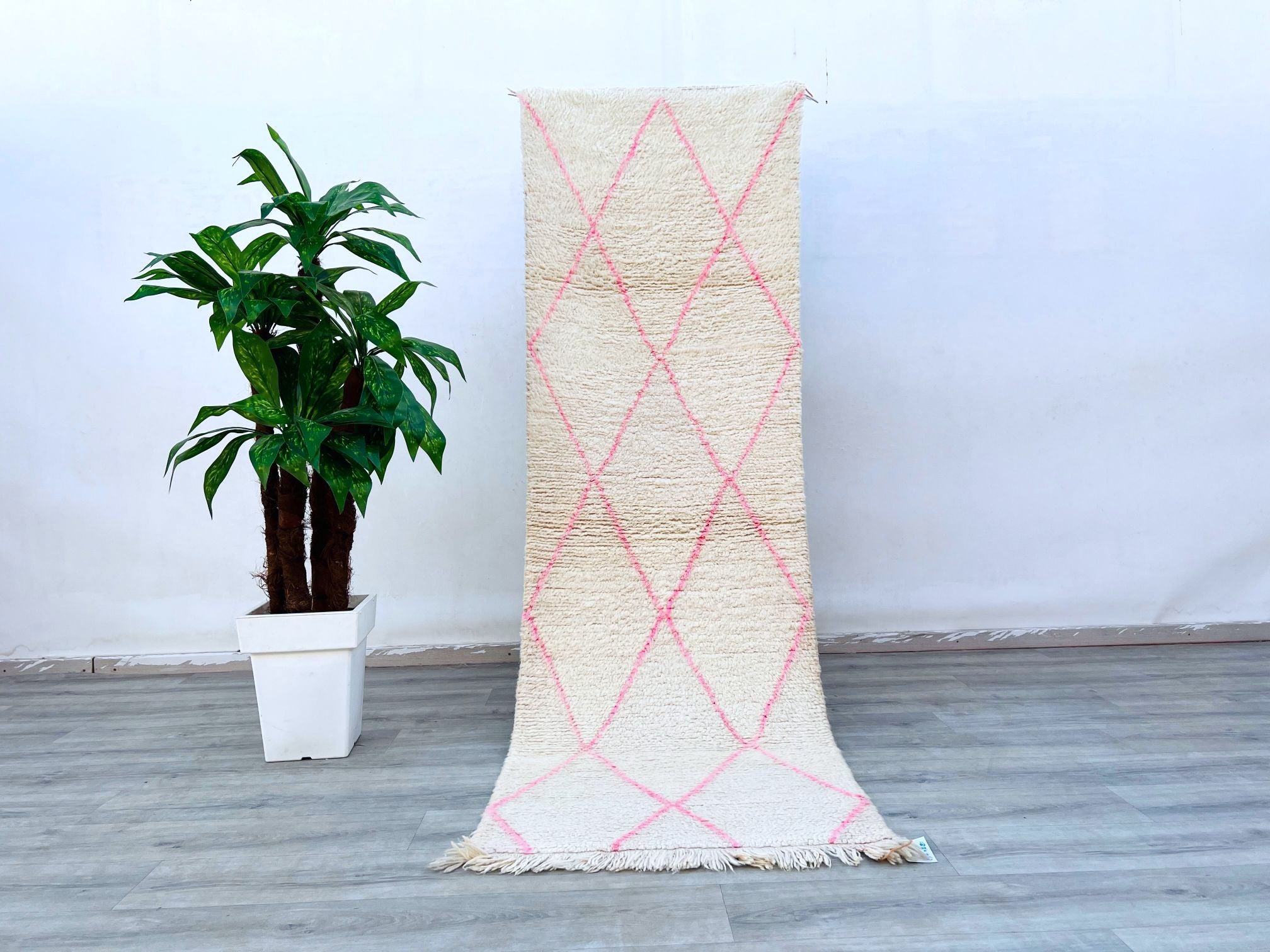 A luxurious pink Beni Ourain runner rug crafted from premium Moroccan wool, designed to elevate your home’s aesthetic with its tribal Berber motifs. This handmade vintage carpet features a soft, high-pile texture, ideal for adding coziness to hardwood or tile floors. The subtle pink and white diamond patterns create a timeless look, perfect for boho-chic, Scandinavian, or eclectic interiors. Measuring 3x8 feet, it fits beautifully in hallways, kitchens, or beside beds as a plush accent rug. Each piece is in