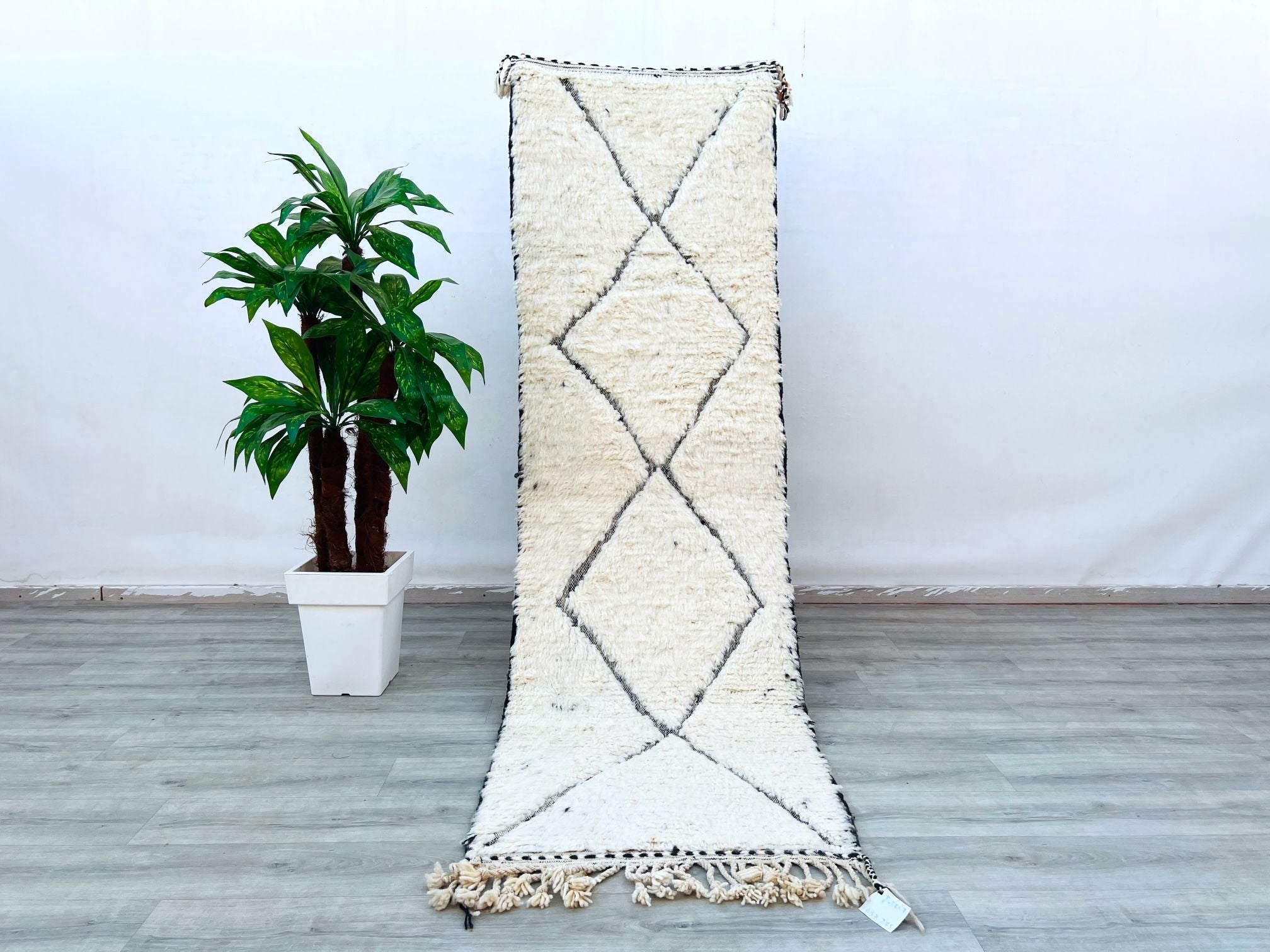 Bring the rich heritage of Morocco into your space with this handwoven Beni Ourain runner rug. Made from premium virgin sheep wool, this 3x10 ft hallway carpet showcases traditional Berber motifs, offering a perfect mix of texture and minimalist charm. The vintage-inspired design features soft ivory tones with subtle geometric patterns, ideal for adding warmth to high-traffic areas. Hand-knotted by artisans using centuries-old weaving methods, this rug is both durable and luxuriously soft. Whether placed in