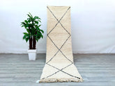 Enhance your home with a handmade Beni Ourain runner rug, crafted by Moroccan artisans using traditional techniques. This long hallway runner (approx. 3x10 FT) features a soft wool texture with classic black-and-white tribal designs, adding warmth and character to any space. The natural undyed wool ensures a hypoallergenic and sustainable choice. Perfect for high-traffic areas, this durable yet cozy Berber carpet works well in modern, Scandinavian, or eclectic interiors. Its versatile neutral tones compleme