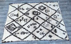 A vintage-inspired Berber wool rug that brings the soul of Morocco into your home. Woven from natural, undyed lamb wool, this Beni Ourain-style carpet features a high-pile shaggy texture for ultimate comfort. The organic ivory-and-charcoal patterns are subtly asymmetrical, celebrating the artistry of handmade imperfections. Ideal for high-traffic areas, the sturdy wool resists wear while maintaining its plush feel. This ethically sourced rug supports women-led cooperatives in rural Morocco, empowering tradi