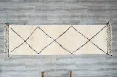 Enhance your home with this authentic Moroccan Berber runner rug (approx. 3x9 FT), handwoven using 100% natural wool for a plush, luxurious feel. The classic Beni Ourain design features subtle blue accents on an ivory background, blending minimalist elegance with tribal charm. Ideal for hallways, kitchens, or as a bedroom accent, this vintage-bound runner is both durable and stylish. Each piece is unique, showcasing slight variations that highlight its artisan craftsmanship. Whether you prefer bohemian, mod