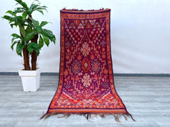 A rare vintage Boujaad rug from Morocco, handcrafted with natural wool and dyed with organic pigments for rich, earthy tones. This oversized Berber carpet (approx. 8x12 ft) showcases intricate diamond and zigzag patterns in deep reds, mauves, and creams, embodying mid-century tribal design. Perfect for Scandinavian, eclectic, or global-inspired interiors, its plush pile and faded vintage appeal add warmth to any space. Each rug tells a story through its handmade imperfections, making it a one-of-a-kind arti