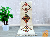 A stunning vintage Moroccan rug handcrafted by Berber weavers, featuring Azilal or Beni Ourain tribal patterns in soft wool. This bohemian area rug showcases organic dyes, abstract symbols, and a plush texture, perfect for layering in living rooms, bedrooms, or entryways. The neutral cream, black, and multicolored accents create a versatile decor piece, while the hand-knotted craftsmanship ensures durability. Each rug tells a story through its unique imperfections and traditional motifs, reflecting Morocco’