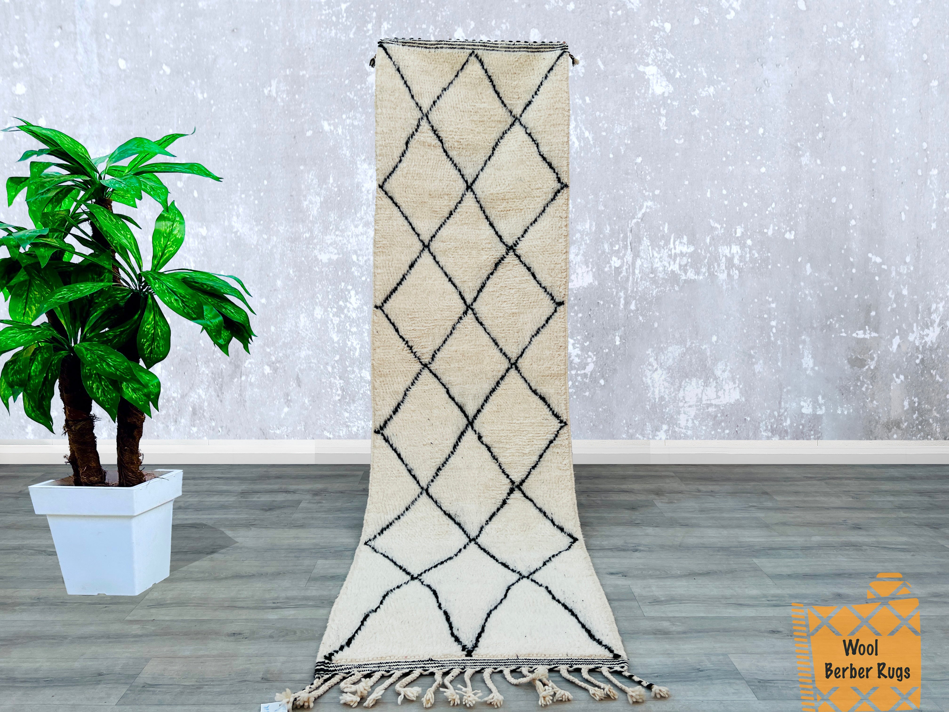 Bring artisanal heritage into your home with this handwoven Beni Ourain Runner Rug, a luxurious Berber wool carpet from Morocco. The soft, high-pile shag texture offers comfort underfoot, while the minimalist black-and-white tribal motifs create a versatile boho-chic aesthetic. Ideal for hallways, kitchens, or lounges, this 3x10 ft vintage Moroccan rug is durable, hypoallergenic, and naturally stain-resistant. Each piece is unique, showcasing traditional Amazigh craftsmanship. Whether layered over hardwood