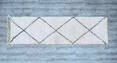 Bring a touch of Moroccan elegance into your home with this handwoven Beni Ourain runner rug. Measuring around 2.9 FT x 9.6 FT, it’s an ideal fit for narrow spaces like hallways, staircases, or beside beds. The intricate Berber motifs in creamy white and dark charcoal reflect centuries-old weaving traditions. Made from 100% natural wool, this rug is breathable, soft, and long-lasting. Its minimalist yet artistic design suits boho, farmhouse, or contemporary decor. Each piece is one-of-a-kind, with slight im