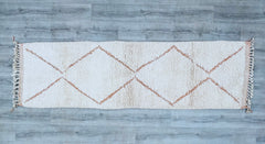 Elevate your hallway or staircase with this exquisite handmade Moroccan Beni Ourain runner rug, crafted from 100% natural wool. Measuring 2.5x9.4 feet, this bespoke long runner features the iconic geometric Berber patterns in a timeless ivory and brown palette. Each rug is hand-knotted by skilled artisans, ensuring durability and a plush, soft texture underfoot. Perfect for high-traffic areas, this vintage-inspired design adds warmth and authenticity to modern or bohemian interiors. The neutral tones blend