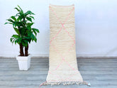 Bring timeless charm into your home with this handmade Moroccan runner rug, featuring a soft pink and ivory checkered pattern inspired by traditional Beni Ourain designs. Woven by skilled artisans using premium wool, this vintage-style Berber rug is both durable and luxuriously soft. The neutral tones and geometric motifs make it a versatile addition to any décor—whether placed in a hallway, bedroom, or lounge area. Measuring 2.3 ft x 9.2 ft, this authentic Moroccan carpet is perfect for adding a bohemian t