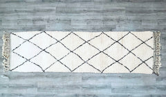 Transform narrow spaces with this exquisite 3 FT x 10 FT Beni Ourain hallway runner, handwoven by Moroccan artisans using premium sheep’s wool. The classic ivory-and-black geometric design adds elegance to corridors, kitchens, or dining rooms, while the thick, plush pile provides comfort and insulation. This eco-friendly, hand-knotted rug showcases the Berber tribe’s signature craftsmanship, with subtle imperfections that highlight its authenticity. Lightweight yet durable, it’s easy to layer over hardwood