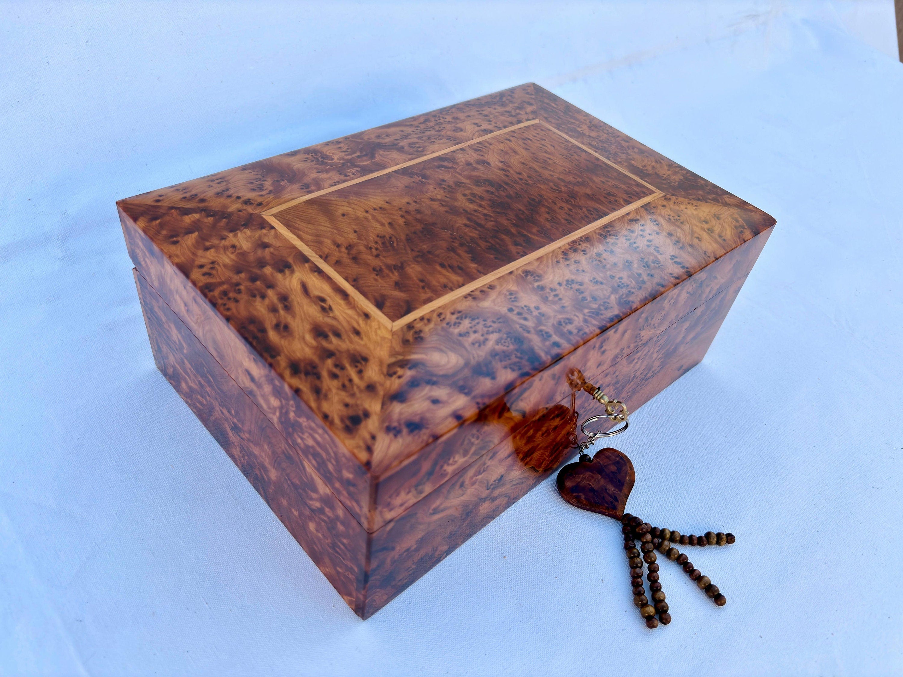 Enhance your jewelry collection with this beautifully handcrafted wooden jewelry box featuring a secure lock. Made from luxurious burl wood, this decorative box showcases intricate natural grain patterns, adding a touch of sophistication to any dresser or vanity. The spacious interior includes two levels of storage, perfect for organizing rings, necklaces, earrings, and watches. The hinged lid and durable latch ensure your valuables stay safe, while the polished finish highlights the wood’s rich texture. Id