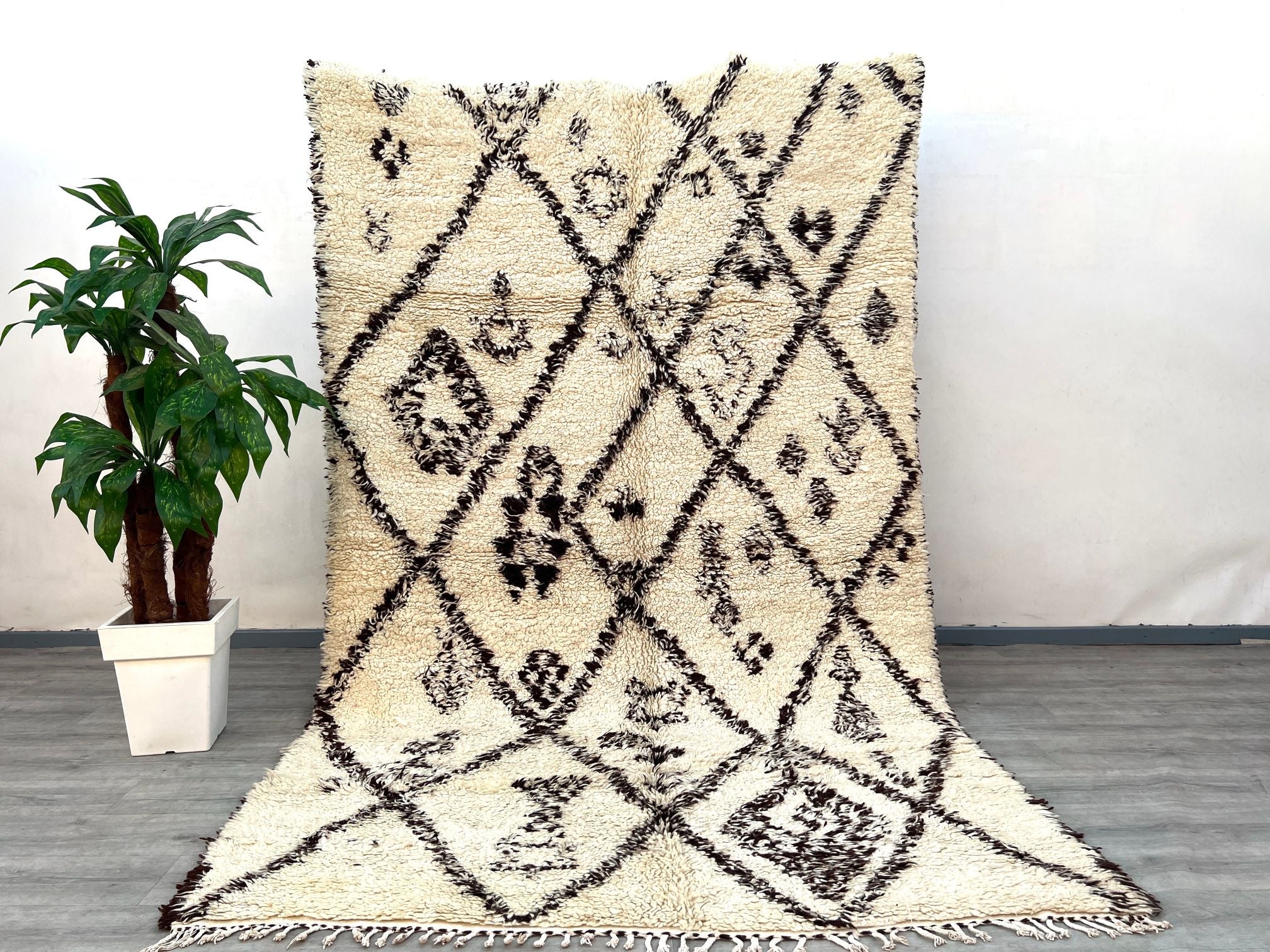 A vintage-inspired Berber wool rug that brings the soul of Morocco into your home. Woven from natural, undyed lamb wool, this Beni Ourain-style carpet features a high-pile shaggy texture for ultimate comfort. The organic ivory-and-charcoal patterns are subtly asymmetrical, celebrating the artistry of handmade imperfections. Ideal for high-traffic areas, the sturdy wool resists wear while maintaining its plush feel. This ethically sourced rug supports women-led cooperatives in rural Morocco, empowering tradi