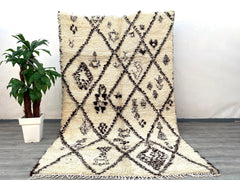 A vintage-inspired Berber wool rug that brings the soul of Morocco into your home. Woven from natural, undyed lamb wool, this Beni Ourain-style carpet features a high-pile shaggy texture for ultimate comfort. The organic ivory-and-charcoal patterns are subtly asymmetrical, celebrating the artistry of handmade imperfections. Ideal for high-traffic areas, the sturdy wool resists wear while maintaining its plush feel. This ethically sourced rug supports women-led cooperatives in rural Morocco, empowering tradi