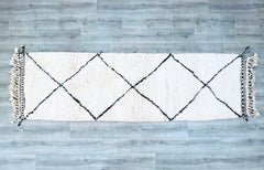 A luxurious handmade Beni Ourain runner rug that combines traditional Berber craftsmanship with modern boho aesthetics. Woven from premium natural wool, this 3x10 ft hallway runner features a classic black-and-white geometric motif, adding texture and sophistication to any space. The thick, plush pile offers ultra-soft comfort, ideal for barefoot walking in entryways, living rooms, or bedrooms. Each rug is one-of-a-kind, with subtle imperfections that highlight its artisan-made authenticity. Perfect for boh