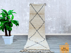 This exquisite Beni Ourain Moroccan Runner Rug (2.9 FT x 9.6 FT) is a handmade wool masterpiece, crafted by skilled Berber artisans. Featuring a soft, high-pile texture in a timeless blue and ivory geometric pattern, this vintage-inspired hallway runner adds warmth and authenticity to any space. Perfect for entryways, living rooms, or bedrooms, its durable, natural wool construction ensures both comfort and longevity. The tribal designs reflect traditional Moroccan heritage, making it a unique boho-chic acc