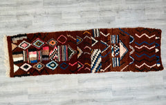 This handmade Berber runner rug (2.5 ft x 8.9 ft) is a stunning vintage Moroccan carpet, ideal for narrow spaces. Featuring a classic tribal motif in warm brown shades, it’s woven from premium wool for lasting resilience and comfort. The rug’s distressed finish highlights its heritage, making it a conversation starter in entryways, dining areas, or offices. Ethically crafted using age-old techniques, it supports traditional artisans while adding organic texture to modern or boho-chic interiors. A practical