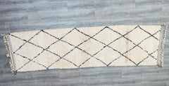 Upgrade your interior with this authentic Moroccan Beni Ourain runner rug, meticulously handwoven from natural wool for a luxurious, textured finish. This long hallway carpet (2.7 FT x 10.0 FT) features a traditional Berber design with black and white geometric patterns, perfect for adding a boho-chic or minimalist touch to any room. The high-quality wool ensures durability and comfort, making it ideal for high-traffic areas. Each rug is unique, with subtle variations that reflect its handmade heritage. Whe