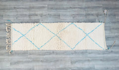 Elevate your home with this authentic handmade Moroccan Beni Ourain runner rug, crafted by skilled Berber artisans. Featuring a stunning blue and beige geometric design, this 2.3 x 7.9 ft vintage hallway runner adds a touch of bohemian elegance to any space. Made from premium sheep wool, this rug is soft, durable, and perfect for high-traffic areas like hallways, entryways, or living rooms. The tribal patterns and natural dyes reflect traditional Moroccan craftsmanship, making it a unique statement piece. W