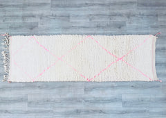 Enhance your home with a stunning handmade Moroccan runner rug, featuring a soft pink Beni Ourain design that adds warmth and elegance to any hallway or corridor. This vintage Berber wool rug is crafted with traditional techniques, showcasing intricate geometric patterns in a bohemian boho style. Measuring 2.7 ft x 8.3 ft, the long, narrow shape is perfect for high-traffic areas, while the 100% natural wool ensures durability and comfort underfoot. The neutral ivory and blush pink tones blend seamlessly wit