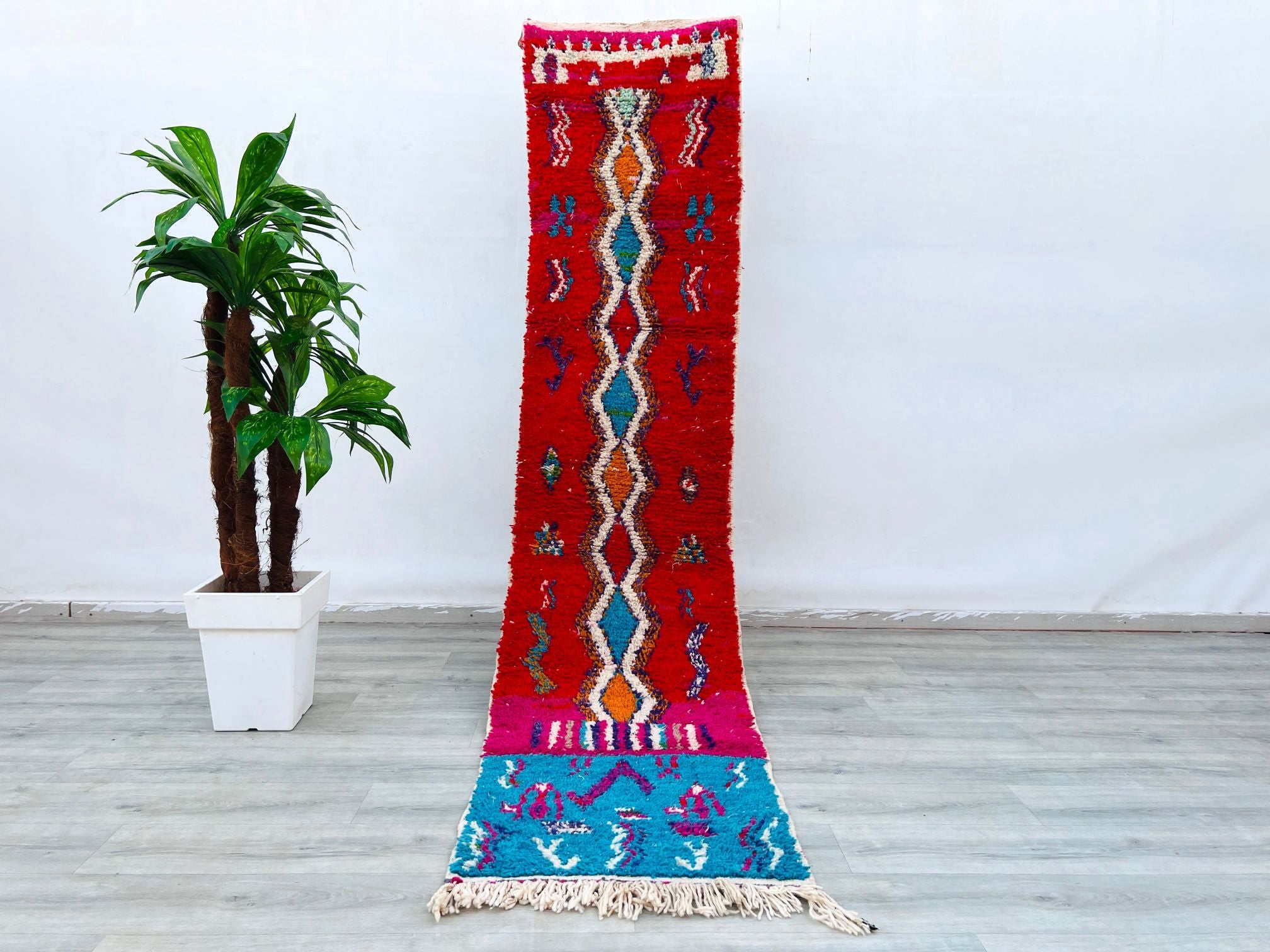 Discover the beauty of a handmade Moroccan tribal rug, crafted using traditional Berber techniques. This vintage runner (2.2x10 ft) features a mix of red, beige, and geometric motifs, inspired by Boujad and Azilal designs. Woven from soft wool, it’s durable yet cozy underfoot, making it perfect for hallways, bedrooms, or layered in bohemian spaces. The distressed, antique finish adds character, while the neutral palette blends seamlessly with modern or rustic decor. Whether you need a statement piece or sub