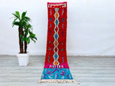Discover the beauty of a handmade Moroccan tribal rug, crafted using traditional Berber techniques. This vintage runner (2.2x10 ft) features a mix of red, beige, and geometric motifs, inspired by Boujad and Azilal designs. Woven from soft wool, it’s durable yet cozy underfoot, making it perfect for hallways, bedrooms, or layered in bohemian spaces. The distressed, antique finish adds character, while the neutral palette blends seamlessly with modern or rustic decor. Whether you need a statement piece or sub
