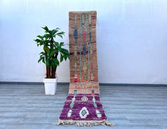 Elevate your décor with this handwoven Berber runner rug, a stunning vintage Moroccan piece measuring 2.3 x 10.9 ft. Crafted from natural wool, it boasts a soft, shaggy texture and a colorful abstract pattern in hues of purple, pink, and cream. The tribal Boujaad design reflects centuries-old weaving traditions, making it a statement piece for boho, eclectic, or minimalist interiors. Ideal for high-traffic areas, this durable yet cozy runner adds warmth to hallways, bedrooms, or entryways. Each rug is one-o