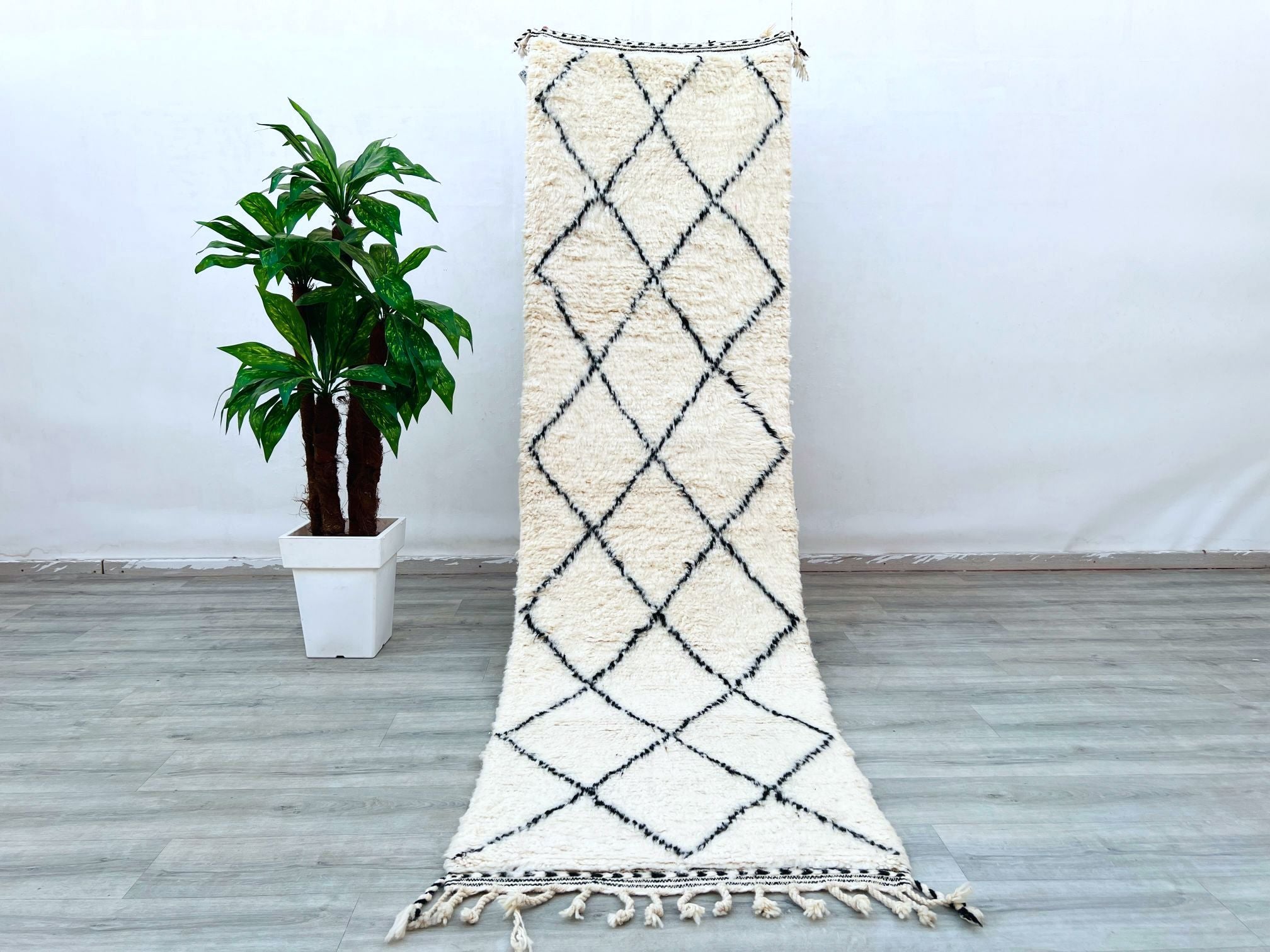 Enhance your home with this long Moroccan Beni Ourain runner rug, featuring a classic black-and-white tribal design. Measuring approximately 3x9 ft, this handmade wool rug is perfect for hallways, kitchens, or living rooms. The Berber craftsmanship ensures a soft yet durable texture, while the vintage-inspired patterns add a touch of bohemian elegance. Made from natural wool, this Moroccan carpet is eco-friendly and non-shedding, making it ideal for high-traffic spaces. Whether layered over hardwood or used