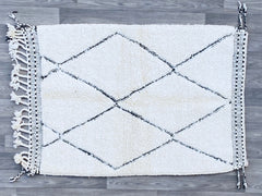 Elevate your décor with this exquisite Beni Ourain rug, a hand-knotted masterpiece from Morocco’s Atlas Mountains. Made from premium undyed wool, this plush, high-pile rug offers unmatched softness underfoot, ideal for cozy living rooms or chic bedrooms. The neutral white and ivory tones with subtle black tribal patterns blend seamlessly into boho, modern farmhouse, or eclectic interiors. Available in multiple sizes (4x6, 5x8, 8x11 ft), this authentic Berber rug is ethically crafted by skilled artisans, ens