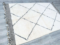 Elevate your space with this minimalist Moroccan wool rug, featuring a clean, neutral design with subtle black geometric accents. Handwoven by artisans, this bohemian-inspired floor decor combines simplicity with artisanal detail, making it a versatile addition to any interior style. The natural wool fibers ensure softness and durability, while the breathable material adapts to different climates. Whether placed in a living room, bedroom, or entryway, this rug brings warmth and sophistication. Its understat