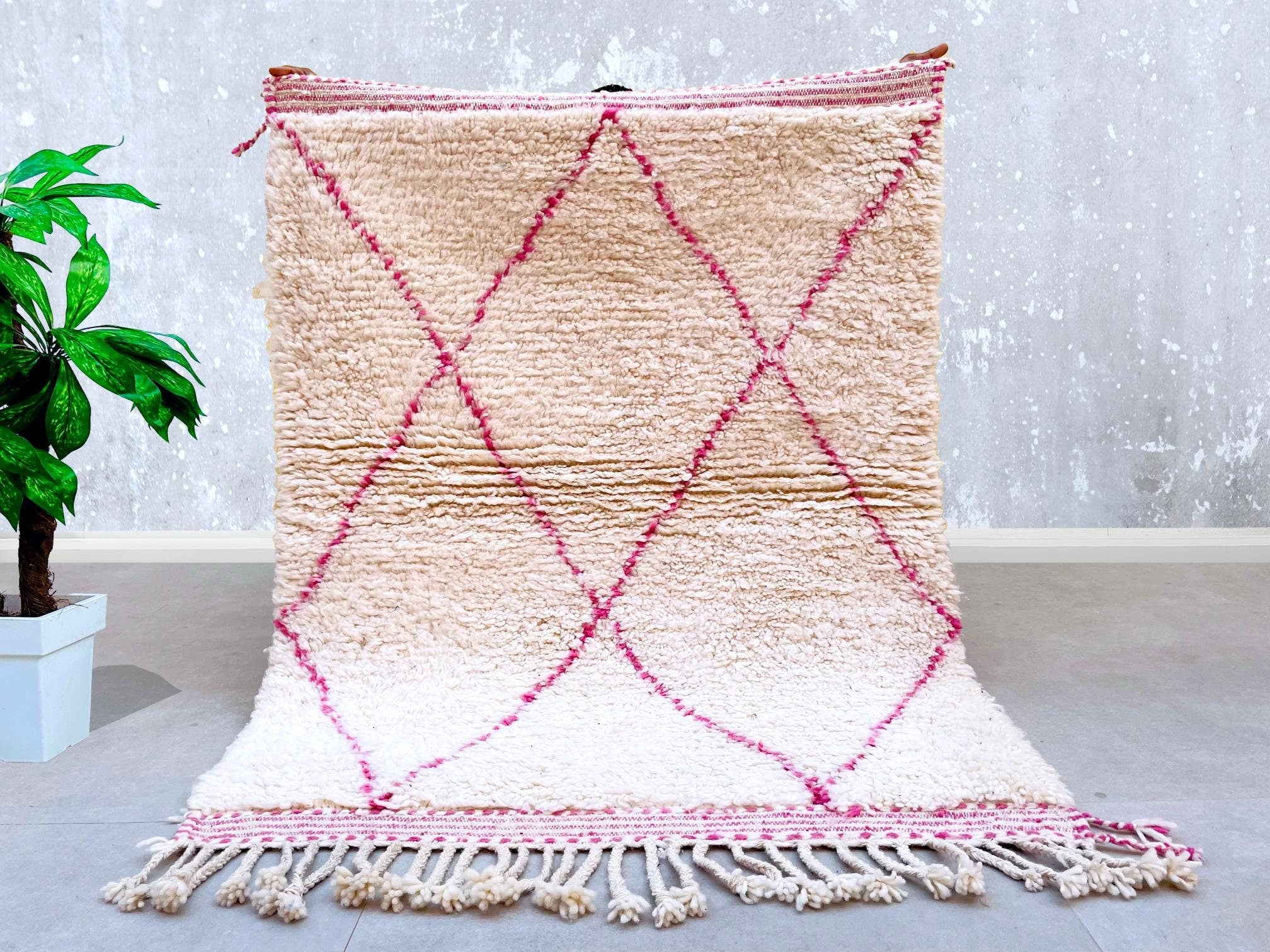 Elevate your interior with this beautiful pink Moroccan rug, inspired by the vibrant Azilal and Beni Ourain weaving traditions. Each piece is meticulously handwoven using natural wool, ensuring a soft yet durable texture. The abstract diamond patterns and geometric lines reflect authentic Berber artistry, creating a unique focal point for any room. Ideal for boho, eclectic, or modern interiors, this rug adds a pop of color while maintaining a neutral elegance. Its lightweight yet sturdy construction makes i