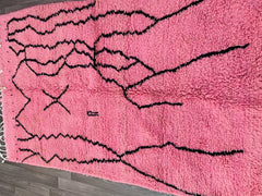 Add a cozy, artistic flair to your home with this hand-knotted Moroccan rug, inspired by the iconic Beni Ourain style. Featuring a soft pink and white palette, this handmade Berber carpet is crafted from natural wool, offering both comfort and durability. The abstract tribal patterns create a visually striking focal point, ideal for boho-chic, Scandinavian, or contemporary interiors. Perfect as a bedside rug, nursery accent, or living room centerpiece, this Azilal-inspired design is ethically made using tra