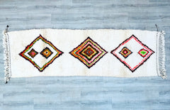 Elevate your home with this handwoven Moroccan Berber runner (3x9 ft), a tribal masterpiece made from 100% natural wool. Featuring Azilal or Beni Ourain designs, this vintage-style rug boasts geometric patterns, faded hues, and a distressed look for a lived-in aesthetic. Perfect for hallways, kitchens, or as a statement floor piece, its durable, soft texture suits high-traffic areas. The ethically handmade craftsmanship ensures authenticity, with no two rugs alike. Whether you prefer neutral tones or bold c