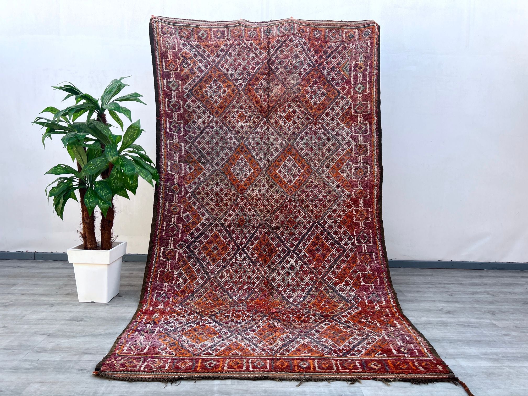 Elevate your interior with this stunning vintage Berber rug, a true testament to Moroccan craftsmanship. Featuring intricate tribal motifs and a distressed, timeworn look, this rug exudes character and cultural heritage. Made from natural sheep wool, it offers both durability and a plush feel underfoot. The faded hues of red, orange, and brown create a warm, inviting atmosphere, perfect for boho, farmhouse, or eclectic-themed spaces. Each knot and weave tells a story of tradition, making this rug not just a