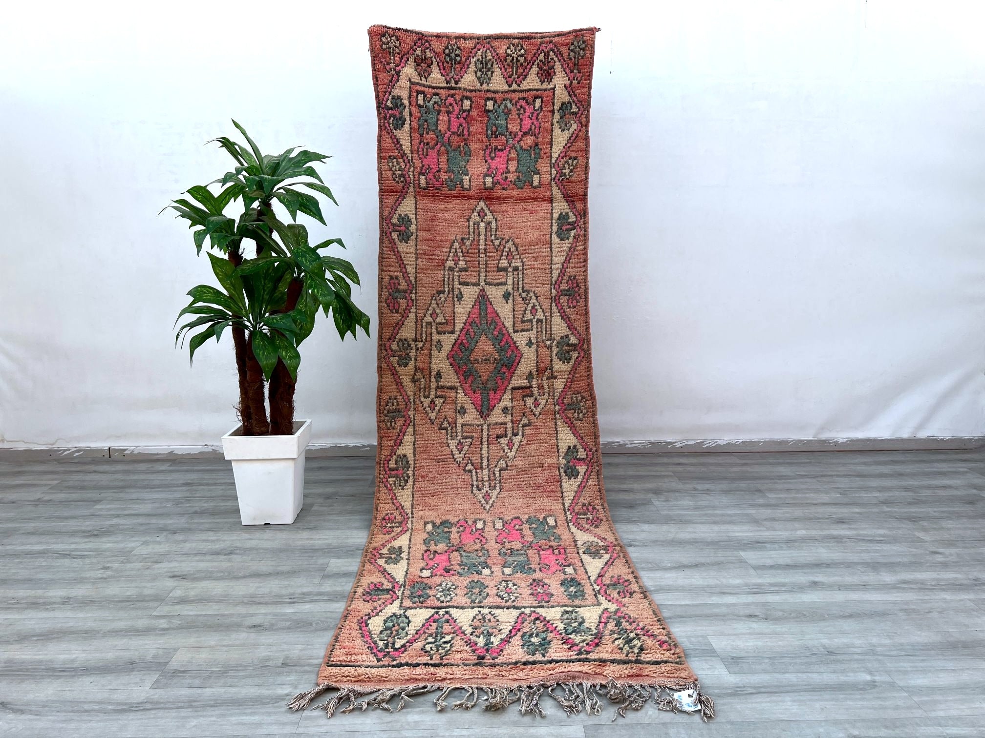 Enhance your hallway with this exquisite light pink vintage Turkish runner rug, measuring 1'10" x 8'9" (9’ft long). Handcrafted from soft wool, this Persian-inspired Herki runner features delicate rose hues and intricate patterns, perfect for adding a touch of bohemian elegance to any space. The distressed vintage look brings character, while the light colors brighten narrow hallways, entryways, or bedroom aisles. Made using traditional techniques, this Turkish rug is durable yet plush underfoot. Ideal for