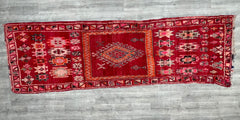 A rare mid-century Moroccan carpet, this 6x12 ft vintage Boujaad rug is a masterpiece of tribal textile art. Featuring bold red and earthy hues, the rug’s hand-knotted wool construction ensures durability and a luxuriously soft feel. The abstract Berber symbols woven into the design carry historical significance, offering a unique conversation piece for any room. Whether used as a statement hallway runner or a bohemian living room centerpiece, this antique Moroccan wool rug brings warmth and authenticity to