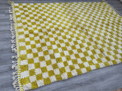 Elevate your interior with this vintage Moroccan wool rug, featuring a classic checkered design in soft yellow and white. Hand-knotted by Berber artisans, this Beni Ourain-style rug combines traditional craftsmanship with a modern geometric pattern, making it a versatile choice for any room. The natural wool fibers provide a plush, cozy feel, ideal for high-traffic areas like living rooms or entryways. Its neutral yet warm tones blend seamlessly with various décor styles, from Scandinavian minimalism to ecl