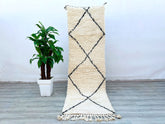 Bring a touch of Morocco into your home with this handmade Beni Ourain runner rug, crafted from 100% natural wool. The 3x8 ft size fits perfectly in hallways, staircases, or as a stylish kitchen runner. Featuring a minimalist white and black tribal pattern, this rug adds texture and elegance to any room. The high-pile wool provides a soft, cozy feel underfoot, while the durable weave ensures long-lasting beauty. Each piece is one-of-a-kind, showcasing traditional Berber weaving techniques. Whether layered o