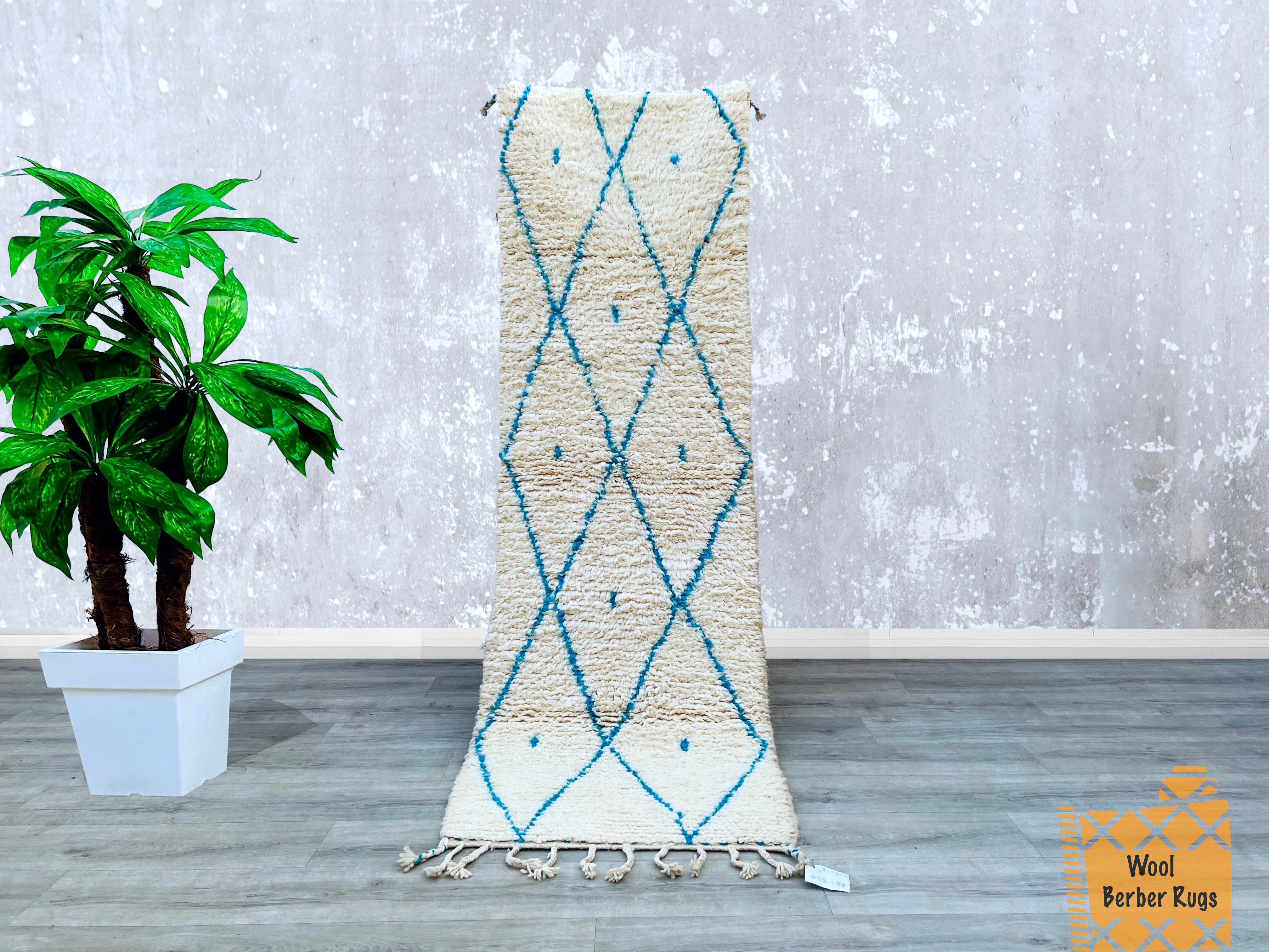 This authentic Moroccan Berber runner rug is a handcrafted masterpiece, showcasing intricate blue diamond motifs on a creamy wool background. Measuring 2.5 x 8 feet, it’s ideal for hallways, kitchens, or living rooms, adding a textured, artisanal touch to your floors. Made using centuries-old weaving techniques, each rug is unique, with slight imperfections that reflect its handmade heritage. The plush, high-pile wool provides comfort underfoot, while the durable, natural fibers ensure longevity. Whether yo
