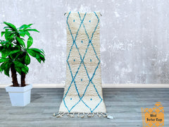 This authentic Moroccan Berber runner rug is a handcrafted masterpiece, showcasing intricate blue diamond motifs on a creamy wool background. Measuring 2.5 x 8 feet, it’s ideal for hallways, kitchens, or living rooms, adding a textured, artisanal touch to your floors. Made using centuries-old weaving techniques, each rug is unique, with slight imperfections that reflect its handmade heritage. The plush, high-pile wool provides comfort underfoot, while the durable, natural fibers ensure longevity. Whether yo