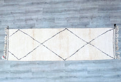 This Beni Ourain runner rug is a handwoven wool masterpiece, showcasing the traditional craftsmanship of Moroccan Berber tribes. The minimalist black-and-white or cream geometric motifs create a stylish, neutral-toned accent for modern and boho interiors. At 2.8 x 9.5 feet, it’s an ideal hallway runner, entryway rug, or long living room carpet. The natural wool is soft yet durable, offering comfort and insulation. Each rug is one-of-a-kind, with slight imperfections that highlight its authentic handmade cha