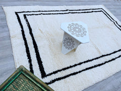Bring a touch of Moroccan heritage into your home with this black and white Beni Ourain-style rug. Meticulously handwoven by Berber artisans, this wool carpet showcases bold geometric patterns against a soft cream background, creating a striking contrast. The high-quality wool ensures durability, while the plush texture adds comfort underfoot. Ideal for contemporary or eclectic interiors, this minimalist yet statement-making rug works beautifully in living rooms, dining areas, or hallways. A perfect blend o