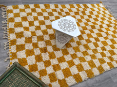 Discover the perfect checkered Moroccan rug in yellow, orange, or neutral tones to brighten your home. These hand-knotted Berber rugs feature a distinctive checkerboard pattern, adding a playful yet sophisticated touch to any room. Made from natural wool and cotton, they are soft underfoot and built to last. Choose from vintage-inspired Azilal rugs, Beni Ourain designs, or modern checkered runners to match your décor. Ideal for bohemian, Scandinavian, or eclectic interiors, these Moroccan checkered rugs are