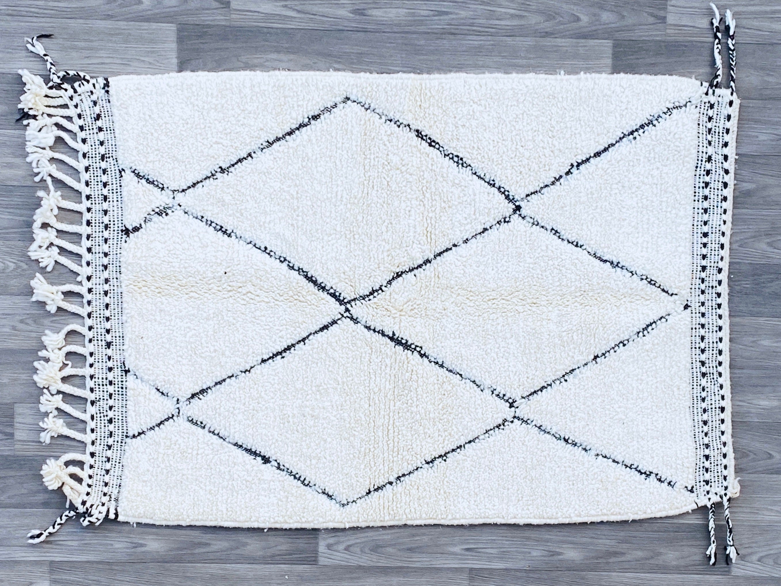 Elevate your décor with this exquisite Beni Ourain rug, a hand-knotted masterpiece from Morocco’s Atlas Mountains. Made from premium undyed wool, this plush, high-pile rug offers unmatched softness underfoot, ideal for cozy living rooms or chic bedrooms. The neutral white and ivory tones with subtle black tribal patterns blend seamlessly into boho, modern farmhouse, or eclectic interiors. Available in multiple sizes (4x6, 5x8, 8x11 ft), this authentic Berber rug is ethically crafted by skilled artisans, ens