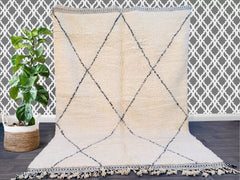 Enhance your space with a vintage Moroccan Berber rug, a stunning handmade wool carpet featuring intricate tribal motifs. Crafted in the classic Beni Ourain tradition, this rug boasts a soft, high-pile texture and an organic, undyed wool finish. The geometric black diamond patterns on a creamy white background create a striking contrast, making it a versatile centerpiece for any room. Perfect for boho-chic, Scandinavian, or eclectic interiors, this authentic Azilal-style rug adds texture and warmth to floor