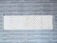 Enhance your floors with a vintage Moroccan Berber runner, a handmade wool rug in classic Beni Ourain style. This long hallway runner (approx. 2.9 FT x 12.5 FT) features organic diamond motifs in ivory and charcoal, ideal for entryways, staircases, or dining rooms. Made from 100% natural wool, it’s durable, hypoallergenic, and sustainably crafted. The minimalist yet bold design suits contemporary, mid-century, or global-inspired interiors. Each rug tells a story through its imperfections and artisanal knots